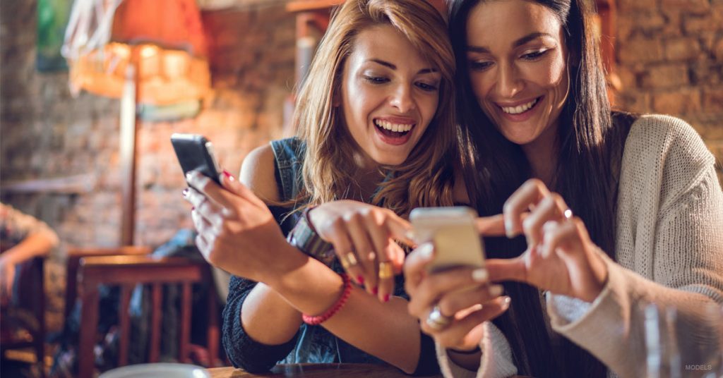 Two young women browsing online and smiling