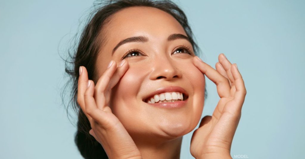 Woman with beautiful skin smiling and lightly touching under her eyes (model)